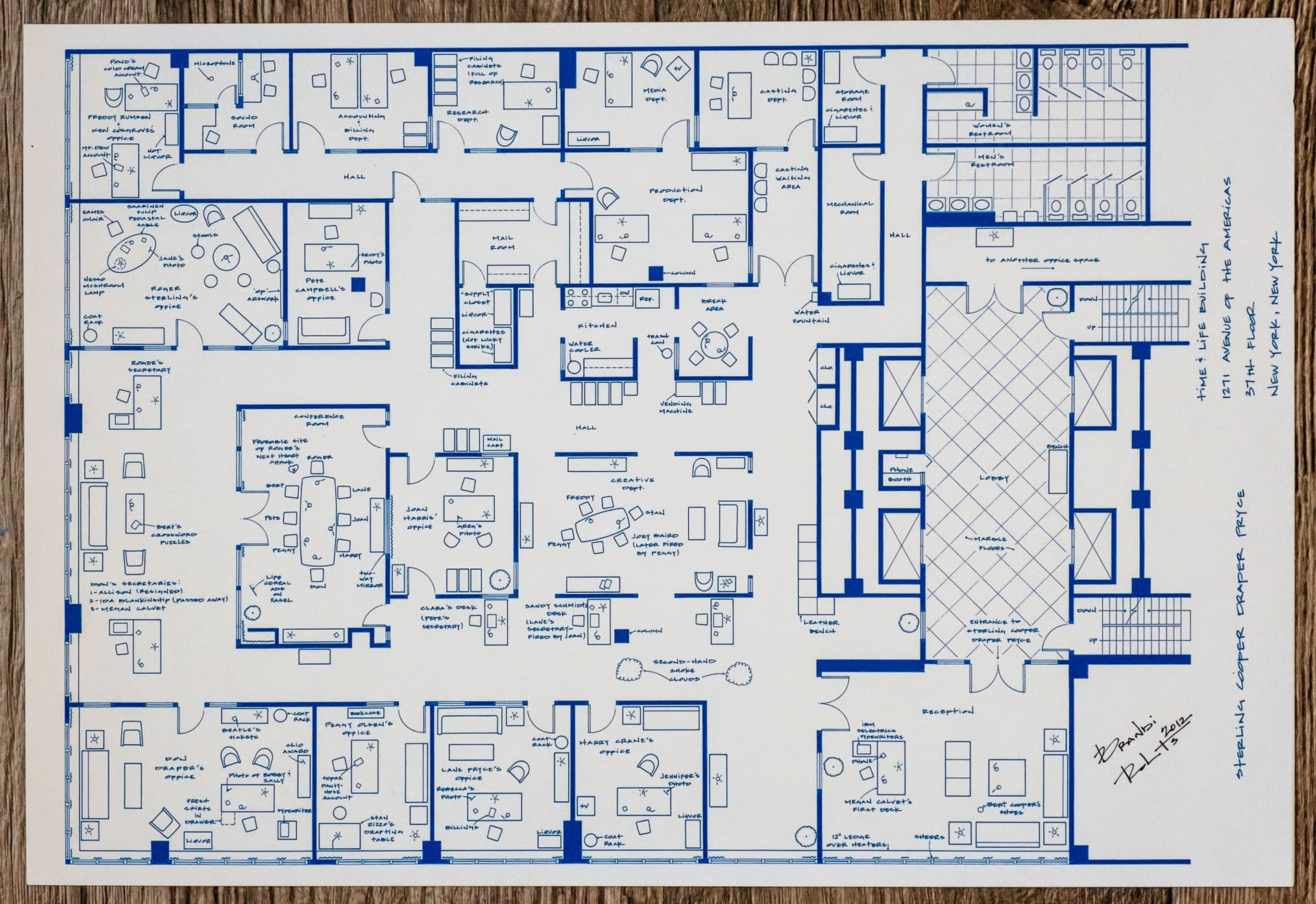 Blueprint floor plan of an office space showing multiple rooms and areas including private offices, conference rooms, reception area, restrooms, and common spaces. The layout features a central hallway with offices and meeting spaces branching off, elevator banks and stairs on the right side, and various workstations throughout. The plan uses blue lines on white background and includes furniture placement within each room.